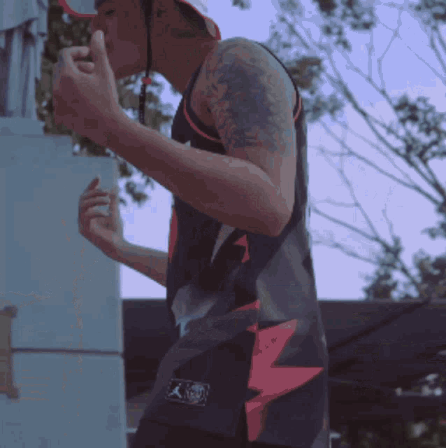 a man with a tattoo on his arm is wearing a black tank top with a red lightning bolt on it