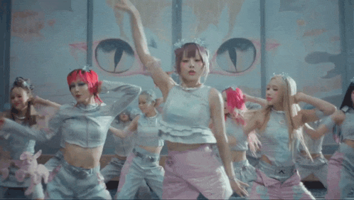 a group of women with pink hair are dancing in front of a cat painting