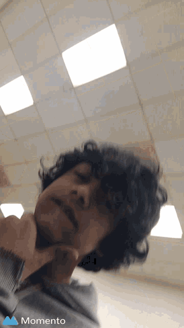 a young man with curly hair is taking a selfie with a momento logo in the corner