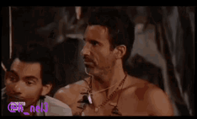 a shirtless man with a necklace around his neck is standing in a cave .