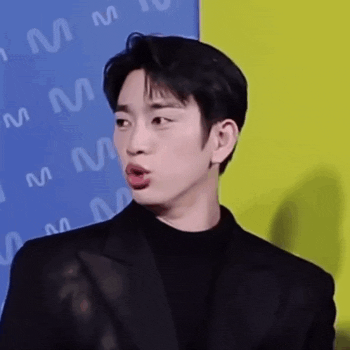 a man in a suit is making a funny face while standing in front of a blue and yellow wall .