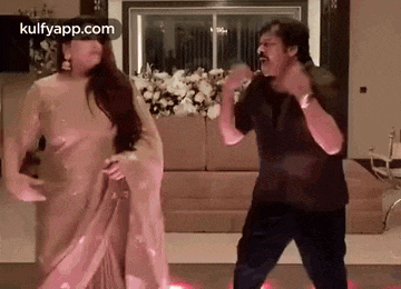 a man and a woman are dancing together in a living room . the woman is wearing a saree .