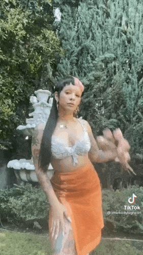 a woman is standing in front of a fountain wearing a crop top and an orange skirt .