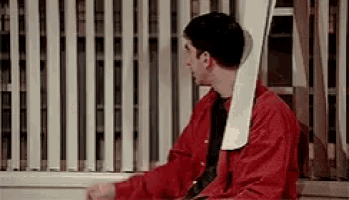 a man in a red shirt and tie is sitting in front of a window with a ladder hanging from his neck .