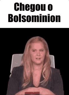 a woman is sitting in a chair with a cell phone in her hand and the words `` chegou o bolsominion '' above her .