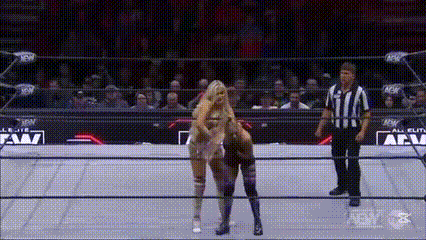 two women are wrestling in a wrestling ring with a referee standing behind them .