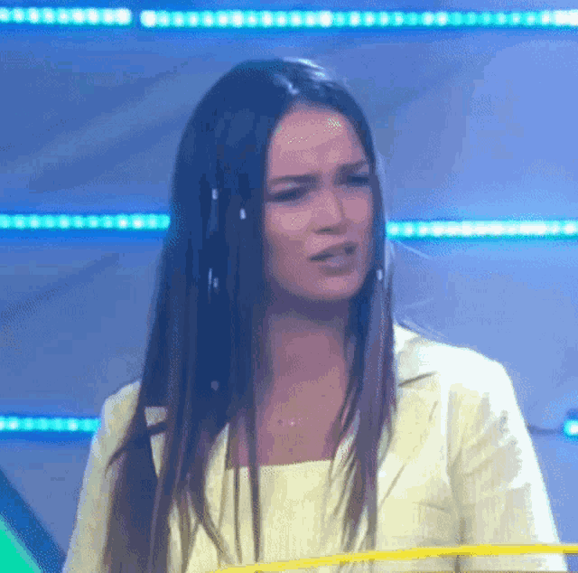 a woman with long hair is wearing a yellow jacket and a white shirt and making a funny face .