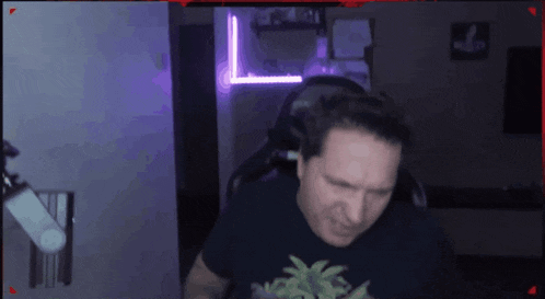 a man wearing a black shirt with a palm tree on it is sitting in a dark room