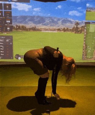 a woman is bending over holding a golf club in front of a screen that says player 1 on it