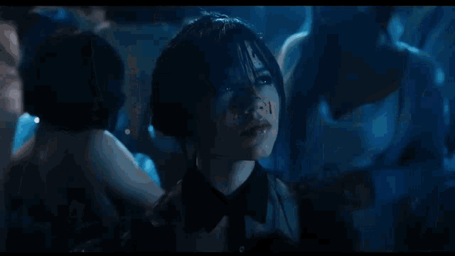 a woman with blood on her face is smiling in a dark room surrounded by other women .