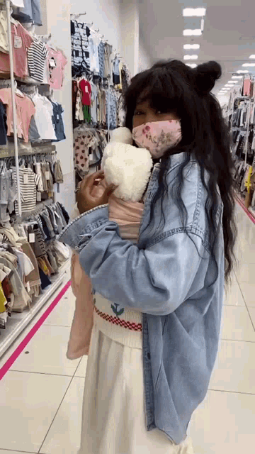a woman wearing a mask is holding a teddy bear in a store .
