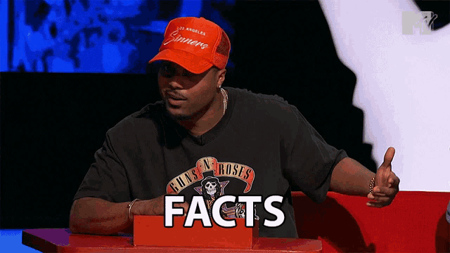 a man wearing a guns n roses shirt sits at a table with a sign that says facts