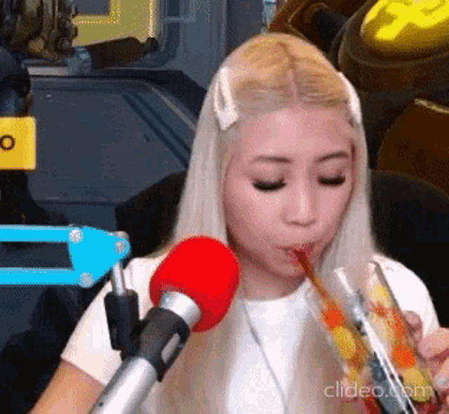 a blonde woman is drinking through a straw from a glass .