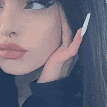 a close up of a woman 's face with a nose ring and a white nail polish .