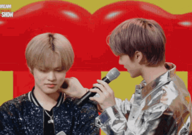 two young men are standing next to each other and one of them is holding a microphone in front of a sign that says dream
