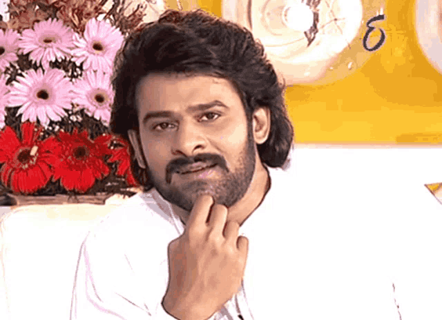 a man with a beard and mustache is looking at the camera with flowers in the background