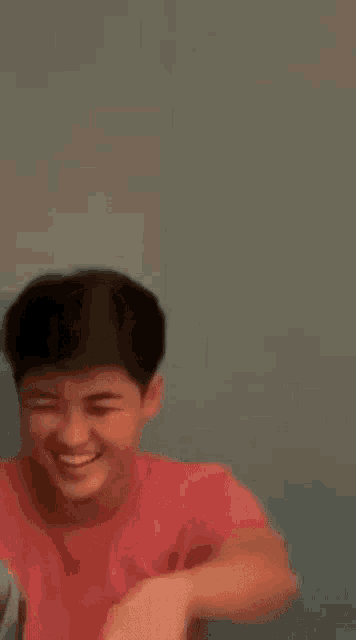 a young man in a pink shirt is smiling and laughing while sitting at a table .