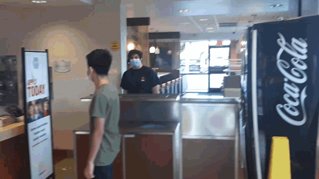 a man wearing a mask stands in front of a coca-cola machine