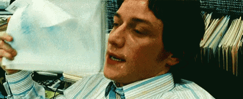 a man in a striped shirt is crying while holding a piece of paper in his hand .