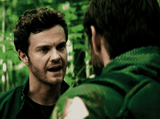 a man with a beard is talking to another man in a green shirt
