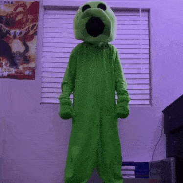 a person in a green monster costume is standing in front of a window with blinds