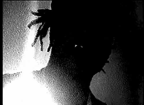 a black and white photo of a person with dreadlocks standing next to a wall .