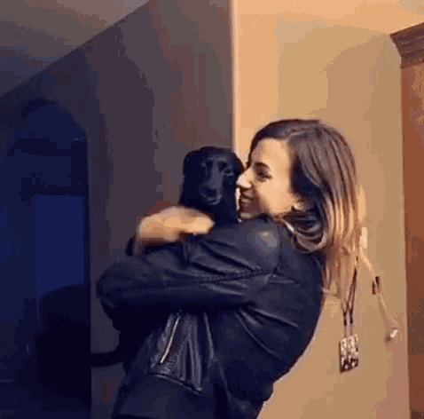 a woman is holding a black dog in her arms .