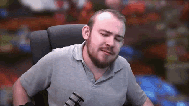 a man with a beard is sitting in a chair with his eyes closed and a microphone in front of him .