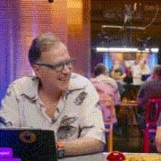 a man wearing glasses sits at a table with a laptop on it