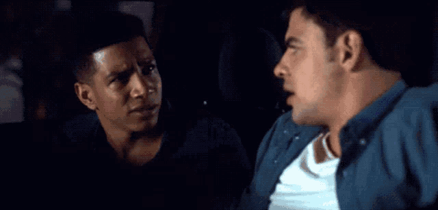 two men are sitting in the back seat of a car and one is looking at the camera