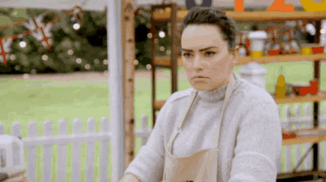 a woman wearing an apron and a sweater looks at something