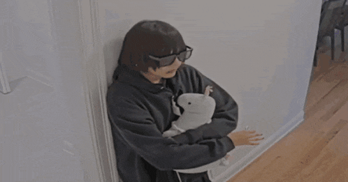 a person wearing sunglasses is holding a stuffed animal while leaning against a wall