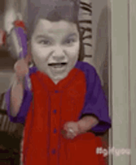a little boy in a red and purple shirt is holding a purple object in his hand .