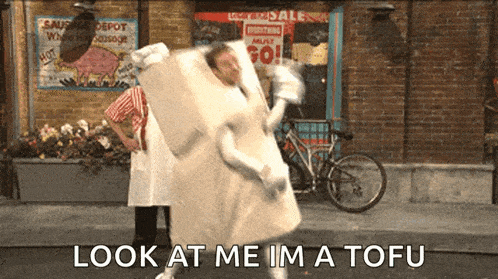 a man in a tofu costume says look at me im a tofu in front of a sausage depot