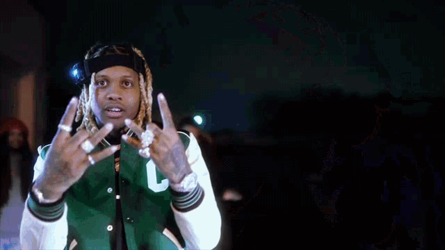 a young man with dreadlocks is wearing a green jacket and a hat .