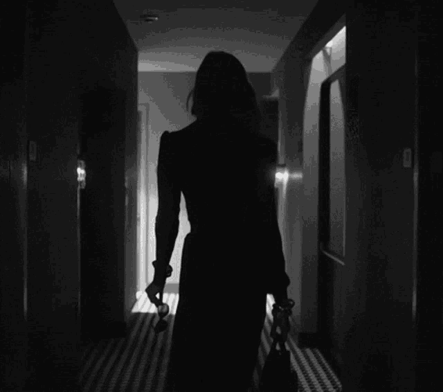 a silhouette of a woman walking down a hallway with a purse