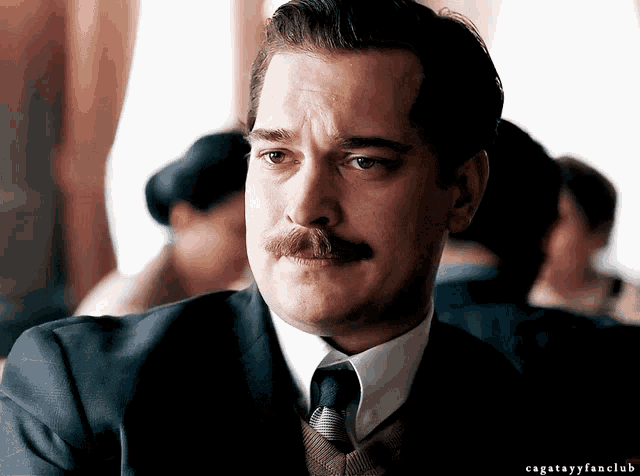 a man with a mustache wearing a suit and tie with the hashtag cagatasyfanclub below him