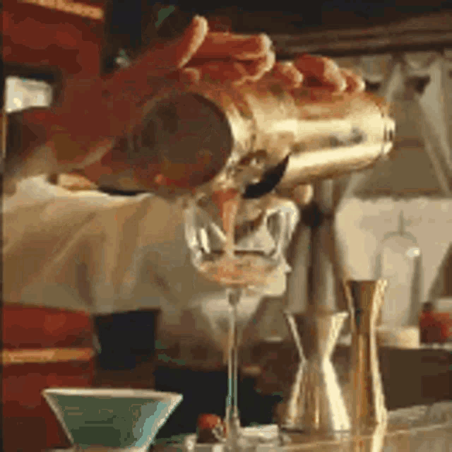 a person is pouring a drink into a martini glass .