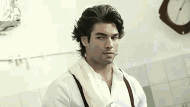 a man in a white shirt and suspenders is standing in front of a clock in a bathroom .