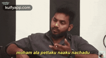 a man with a beard is sitting in front of a white and black wall and says moham ala pettaku naaku nachadu