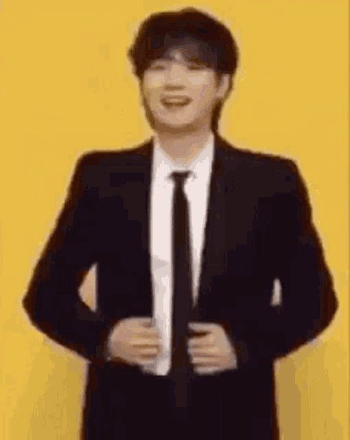 a man in a suit and tie is standing in front of a yellow wall and smiling .