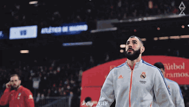 a man in a white adidas jacket stands in front of a sign that says atletico de madrid