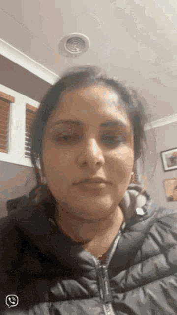 a woman wearing a black jacket and headphones looks at the camera with a phone icon in the corner