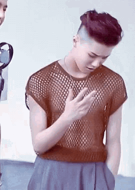 a young man with purple hair is wearing a mesh shirt and a necklace .