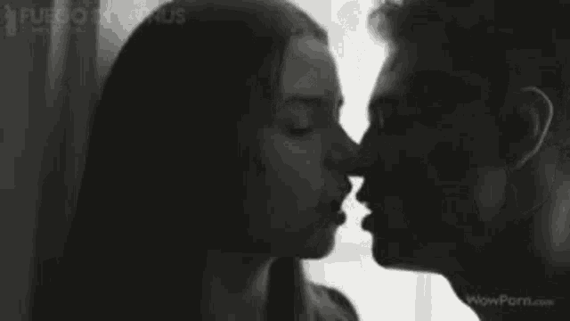 a man and a woman are kissing in front of a window in a black and white photo .