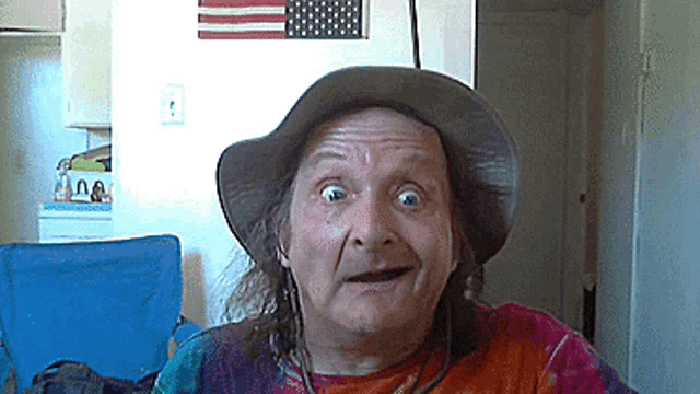 a man wearing a hat and a tie dye shirt makes a funny face