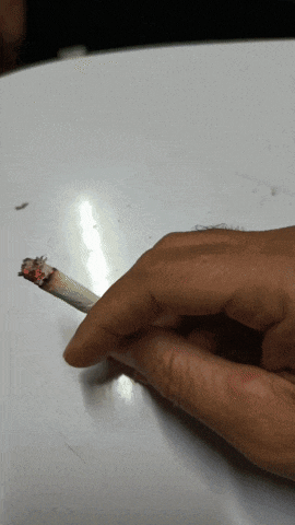 a close up of a person holding a cigarette on a white surface