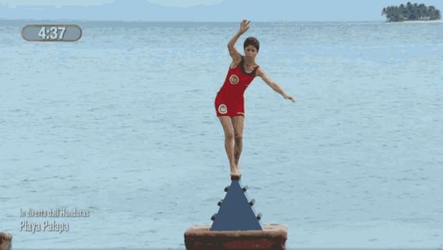 a woman in a red bathing suit is balancing on a blue block in the water with the time 4:37
