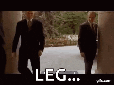two men in suits and ties are walking down a hallway with the words leg written on the screen .