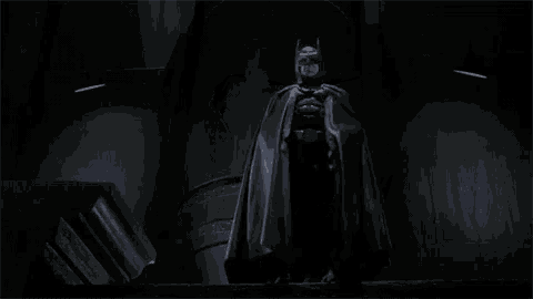 a man in a batman costume is standing in the dark .